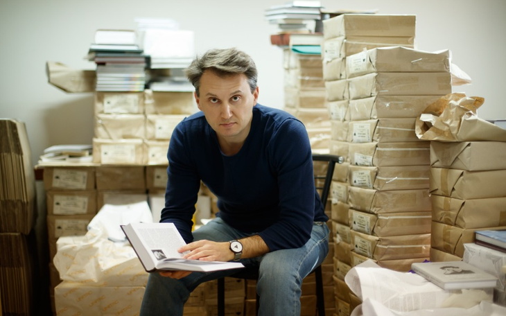 Mężczyzna siedzący wśród stosów książek, skupiony na lekturze.