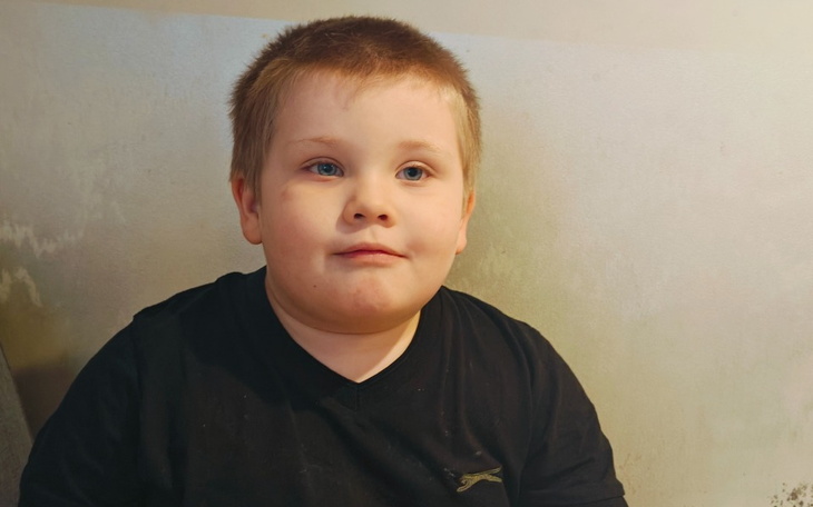 Chłopiec w czarnym t-shircie, siedzący na tle jasnej ściany.