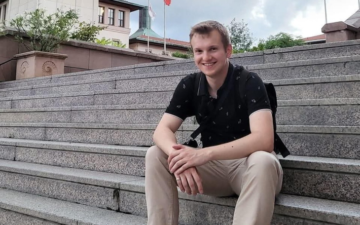 Młody mężczyzna siedzi na schodach z uśmiechem.