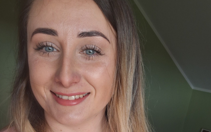 Uśmiechnięta kobieta z długimi włosami, w zielonym tle.