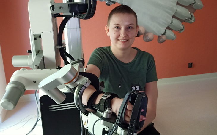 Młoda kobieta z uśmiechem, trzymająca rękę na ramieniu robota.