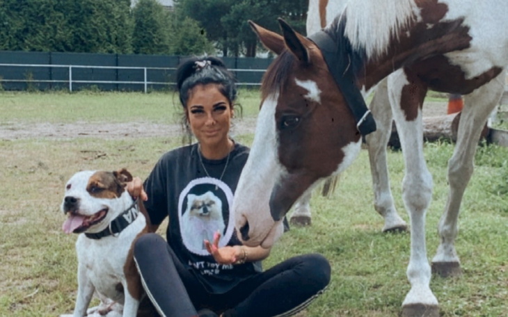 Kobieta z psem i koniem na łące, uśmiechnięta i zrelaksowana.