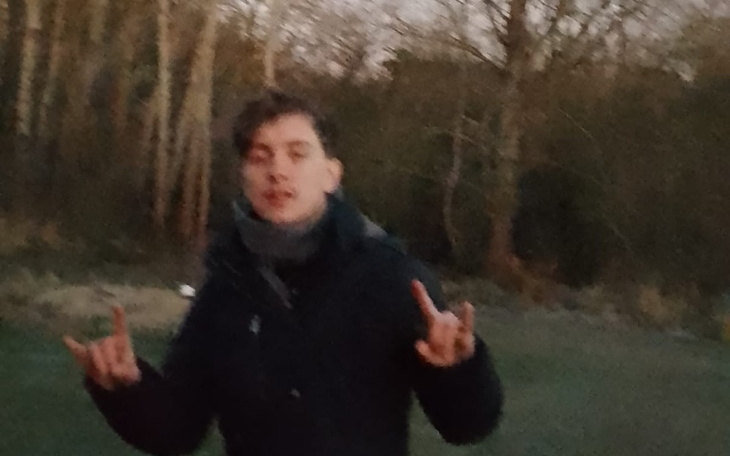 Młody mężczyzna w ciemnym płaszczu, pokazujący znak pokoju.