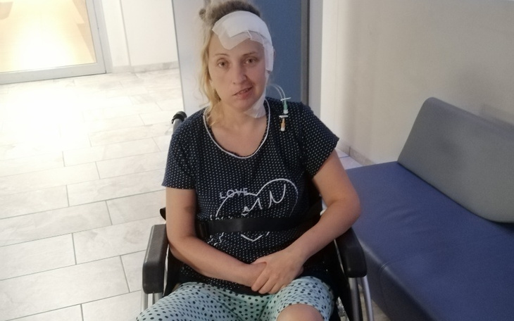 Kobieta na wózku inwalidzkim, z opatrunkiem na głowie.