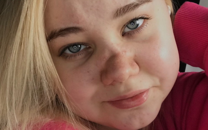 Portret dziewczyny z jasnymi włosami, uśmiechającej się do kamery.