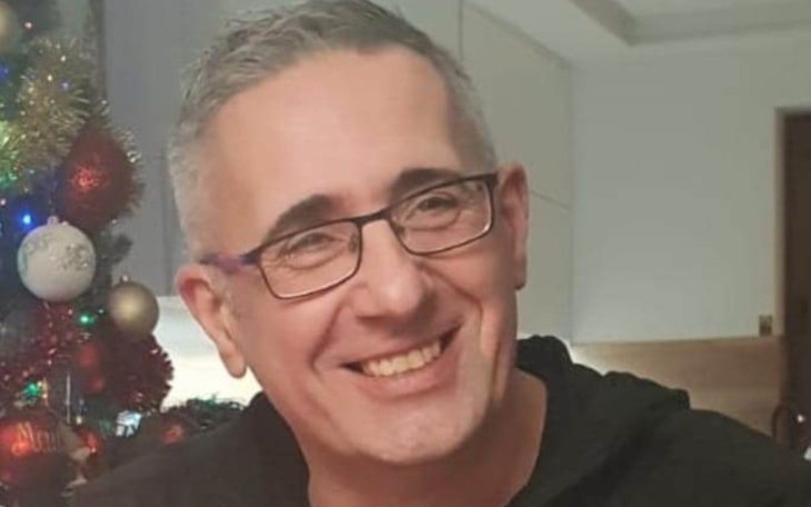 Mężczyzna z uśmiechem, siedzący przy choince.