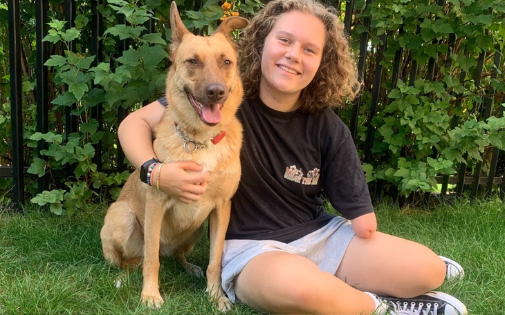 Młoda dziewczyna z psem na trawie, uśmiechnięta i szczęśliwa.