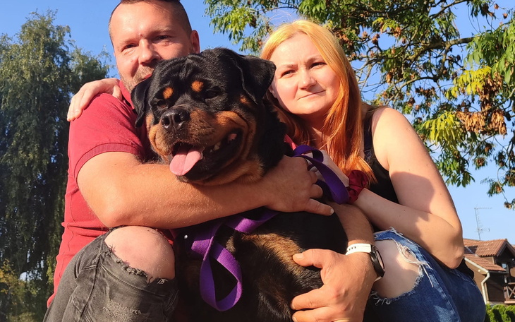 Para z psem rasy Rottweiler, uśmiechnięci w parku.