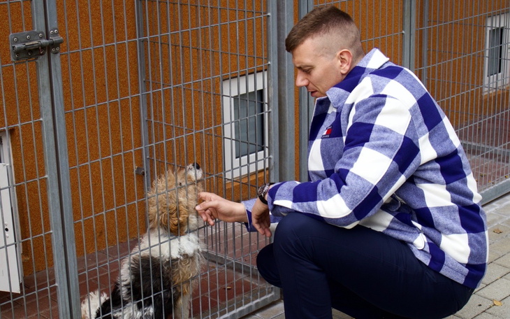 Mężczyzna w kratkę głaszcze psa przez ogrodzenie.