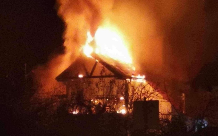 Płonący dom w nocy, ogień wydobywający się z dachu.