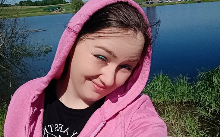 Kobieta w różowej bluzie uśmiecha się nad jeziorem.