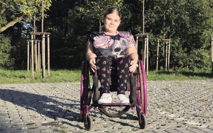 Dziewczyna na wózku inwalidzkim, uśmiechająca się w parku.