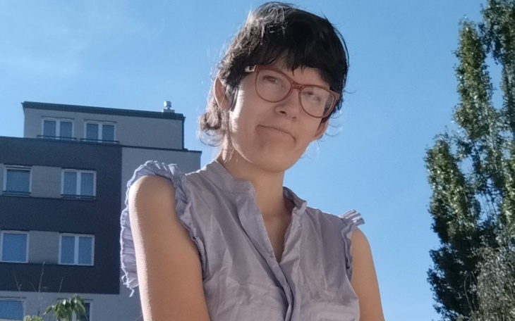 Kobieta w okularach, stoi na tle budynku.