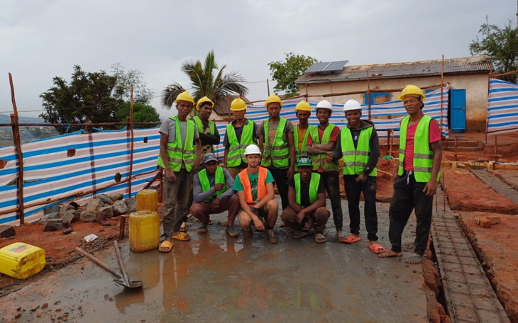 Grupa pracowników budowlanych w kaskach na placu budowy.