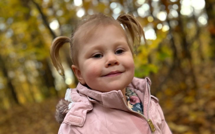 Uśmiechnięta dziewczynka w lesie, w jesiennej scenerii.