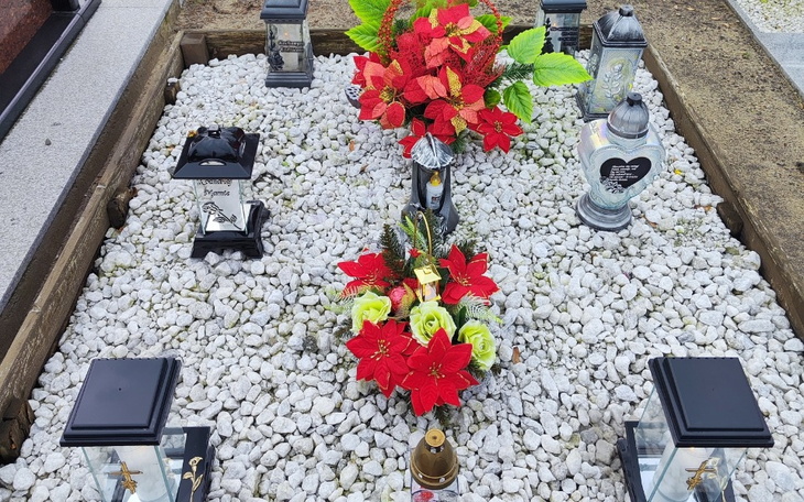Grób ozdobiony kwiatami i zniczami.
