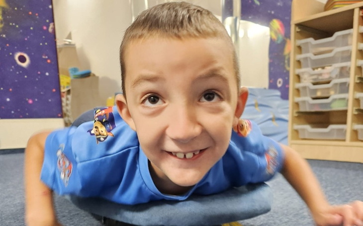 Chłopiec leży na podłodze, uśmiechając się do kamery.