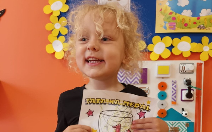 Mała dziewczynka trzyma rysunek z napisem 'Tata na medal'.