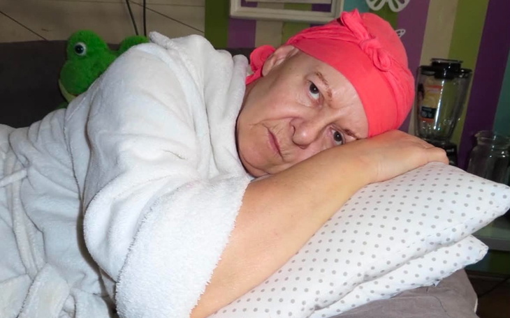 Kobieta w różowej chustce leży na poduszce, wyrażając smutek.