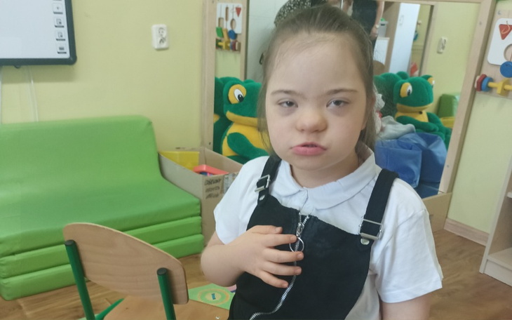 Dziewczynka z zespołem Downa w przedszkolu, z poważnym wyrazem twarzy.