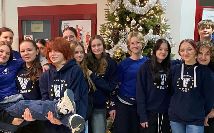 Grupa młodzieży pozująca przed choinką w świątecznym klimacie.