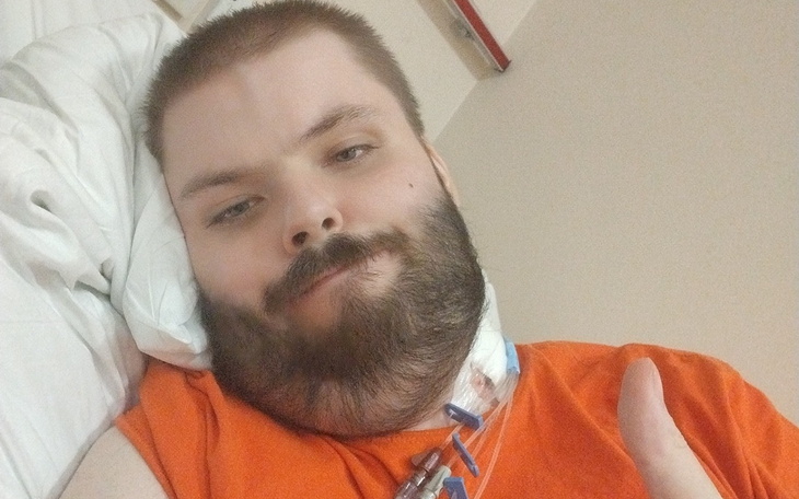 Mężczyzna w szpitalu, leżący na łóżku, pokazujący kciuk w górę.