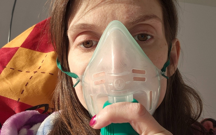 Kobieta z maską tlenową, trzymająca urządzenie w dłoni.