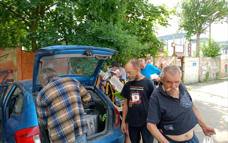 Grupa ludzi przy samochodzie, rozdzielająca jedzenie.