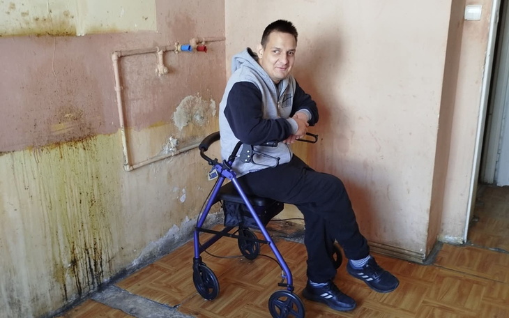 Mężczyzna siedzący na wózku, w prostym wnętrzu.