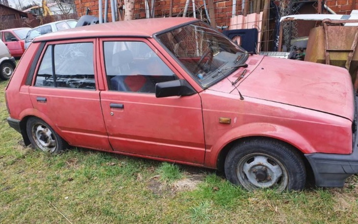 Stary, czerwony samochód zaparkowany na trawie.