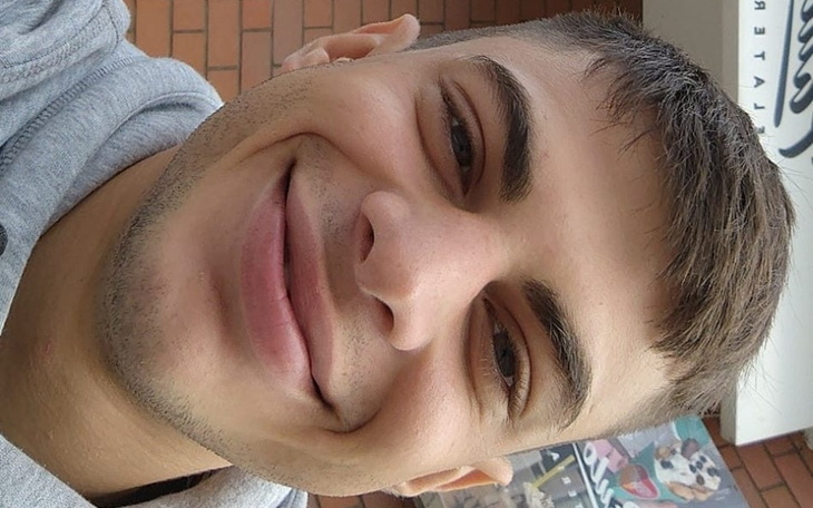 Młody mężczyzna z szerokim uśmiechem, pozujący na zewnątrz.