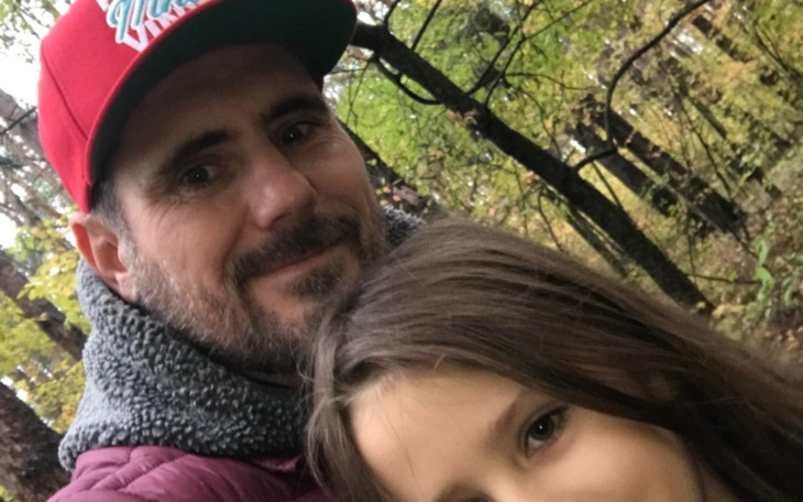 Mężczyzna z dzieckiem w lesie, oboje uśmiechnięci.