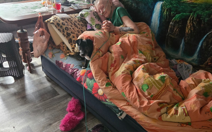 Osoba owinięta w koc, leżąca na kanapie z psem obok.