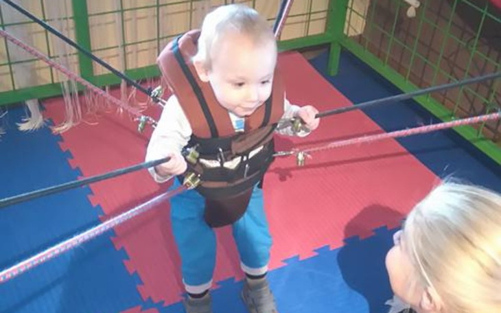 Małe dziecko w uprzęży, bawiące się w specjalnym pomieszczeniu.