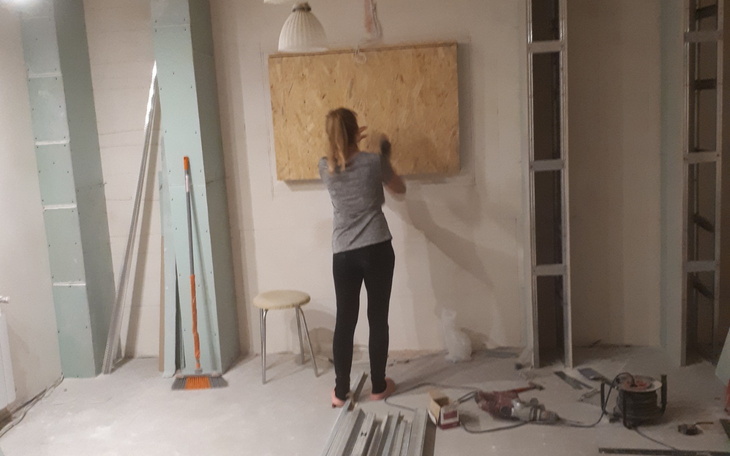 Kobieta pracująca nad drewnianą płytą w remontowanym pomieszczeniu.