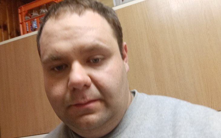 Mężczyzna w szarej bluzie, patrzący w kamerę.
