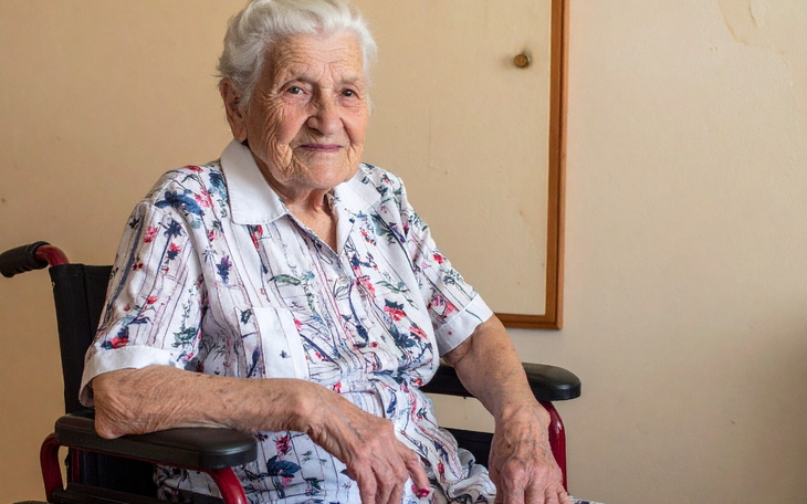 Starsza kobieta siedzi na wózku, uśmiechając się do kamery.