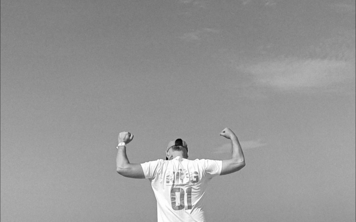 Mężczyzna w białej koszulce, pokazujący mięśnie na tle nieba.