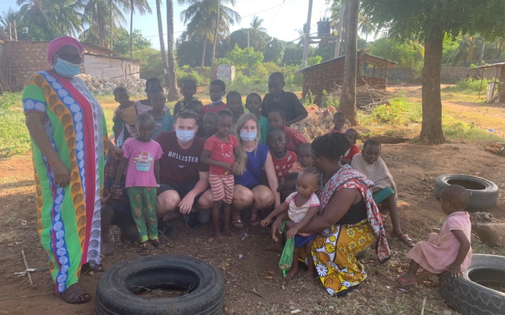 Grupa dzieci z opiekunami w kolorowych strojach na tle natury.