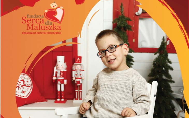 Chłopiec w okularach siedzący w świątecznym otoczeniu.