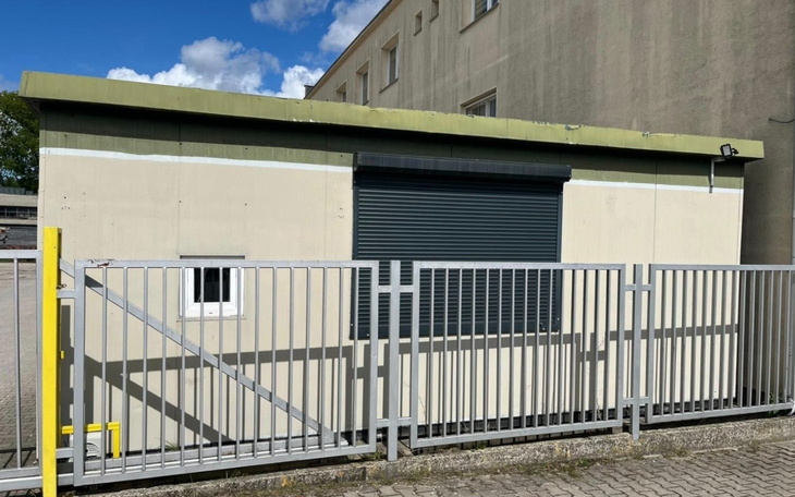 Budynek z zamkniętymi roletami, otoczony ogrodzeniem.