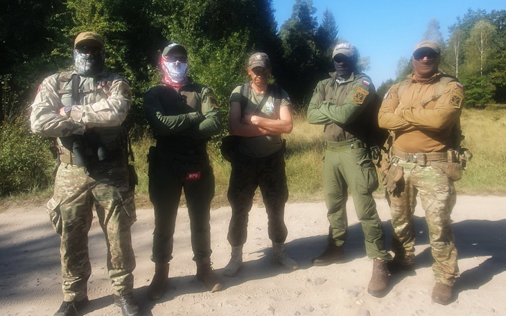 Grupa mężczyzn w mundurach, pozująca do zdjęcia w lesie.