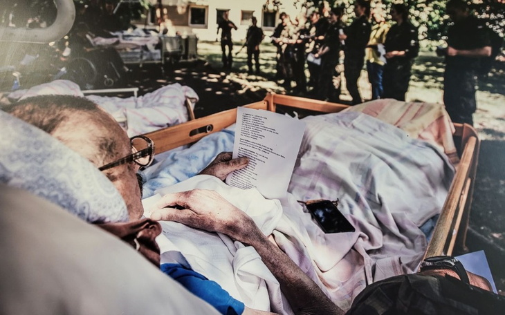 Osoba leżąca w łóżku, trzymająca kartkę z tekstem.