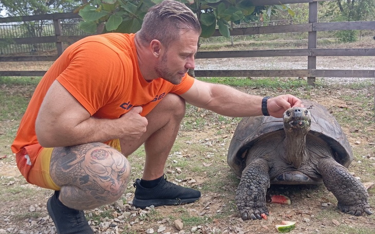 Mężczyzna głaszcze żółwia na świeżym powietrzu, otoczony naturą.