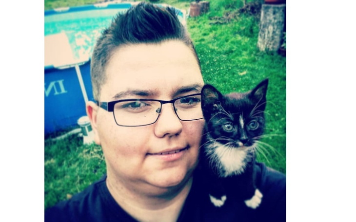 Osoba z kotem na ramieniu, w zielonym otoczeniu.