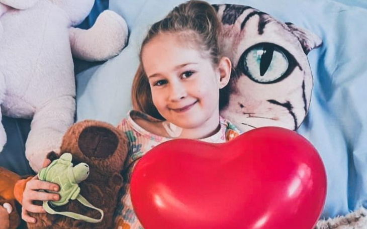 Dziewczynka trzymająca serce, otoczona pluszakami.