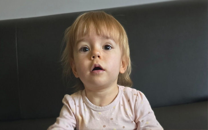 Małe dziecko siedzi na kanapie z zaskoczonym wyrazem twarzy.