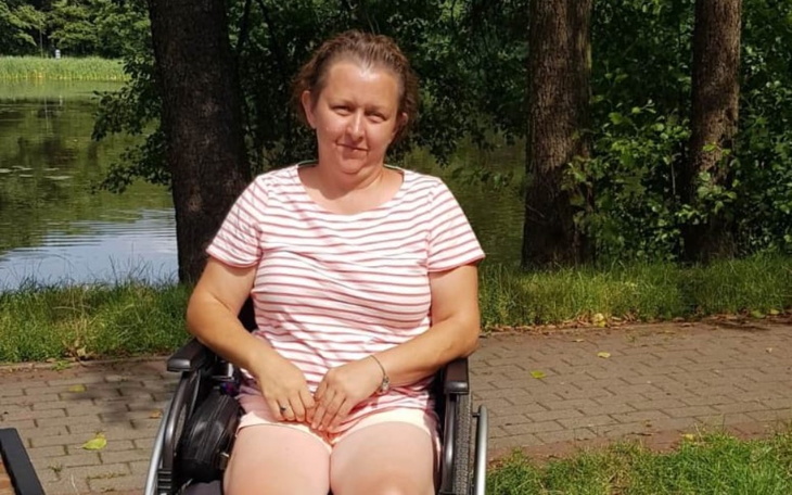 Kobieta na wózku inwalidzkim, siedząca w parku nad jeziorem.