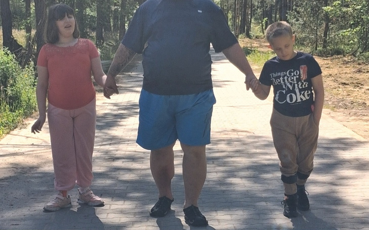 Dzieci trzymające się za ręce, spacerujące z dorosłym w lesie.