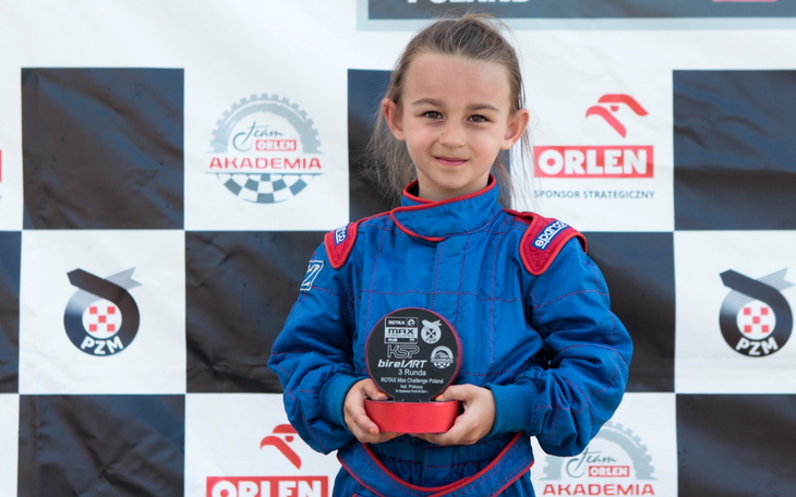 Młoda dziewczynka w kombinezonie wyścigowym z trofeum.